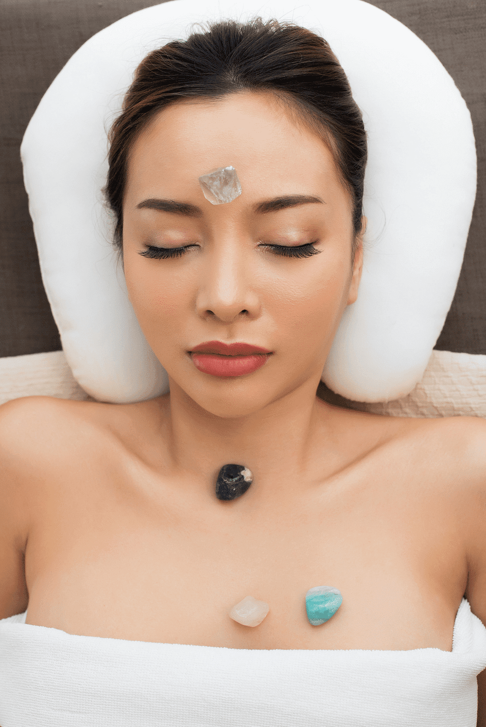 Facial crystal healing therapy with stones on forehead and chest of a relaxed woman.